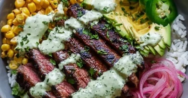 Steak bowl topped with avocado, roasted corn, and cilantro cream sauce.